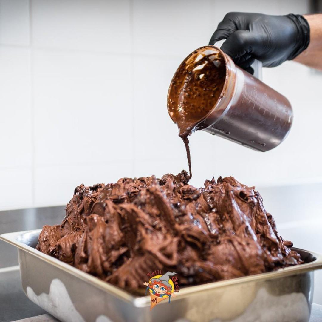 Cioccolato fuso versato a mano da una brocca su una vaschetta di gelato al cioccolato, nel laboratorio