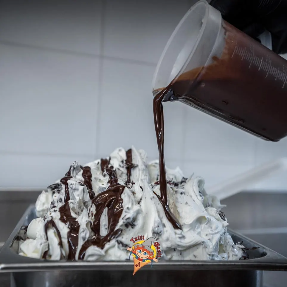 Cioccolato fuso versato da una brocca su una vaschetta di gelato stracciatella nel laboratorio