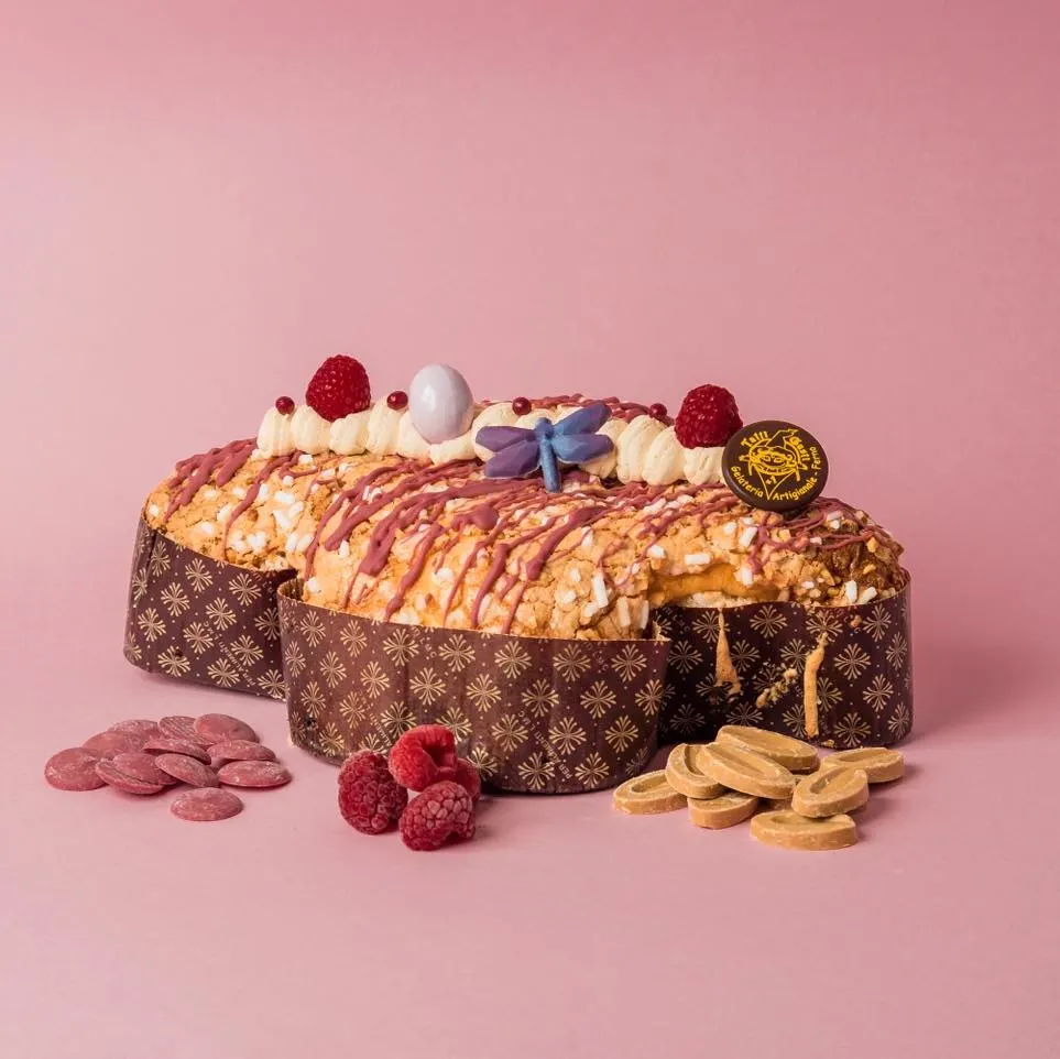 Colomba decorata con panna, lamponi e una libellula di zucchero, su fondo rosa