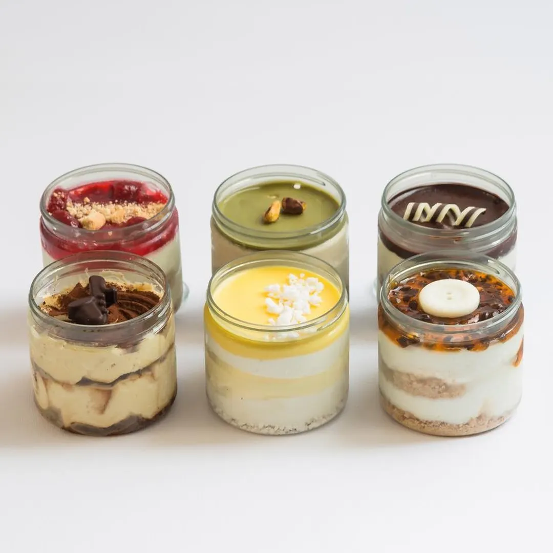 Sei dessert in vasetto di vetro con strati e guarnizioni diverse: frutti rossi, pistacchio, cioccolato, mango