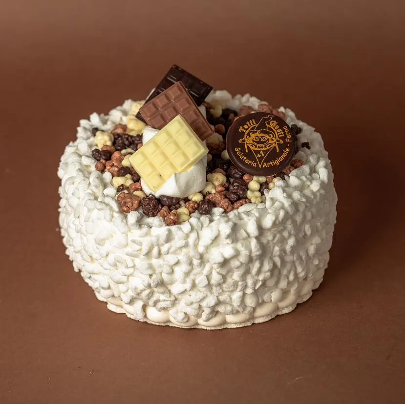 Torta gelato ricoperta di panna con cioccolatini e il disco di cioccolato firmato Tutti Gusti +1, su fondo cacao
