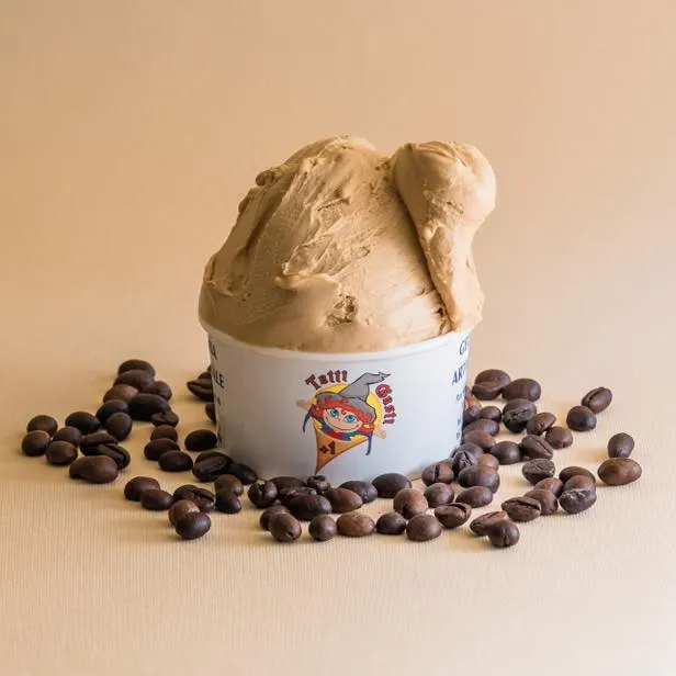 Coppetta di gelato al caffè circondata da chicchi di caffè, su fondo crema