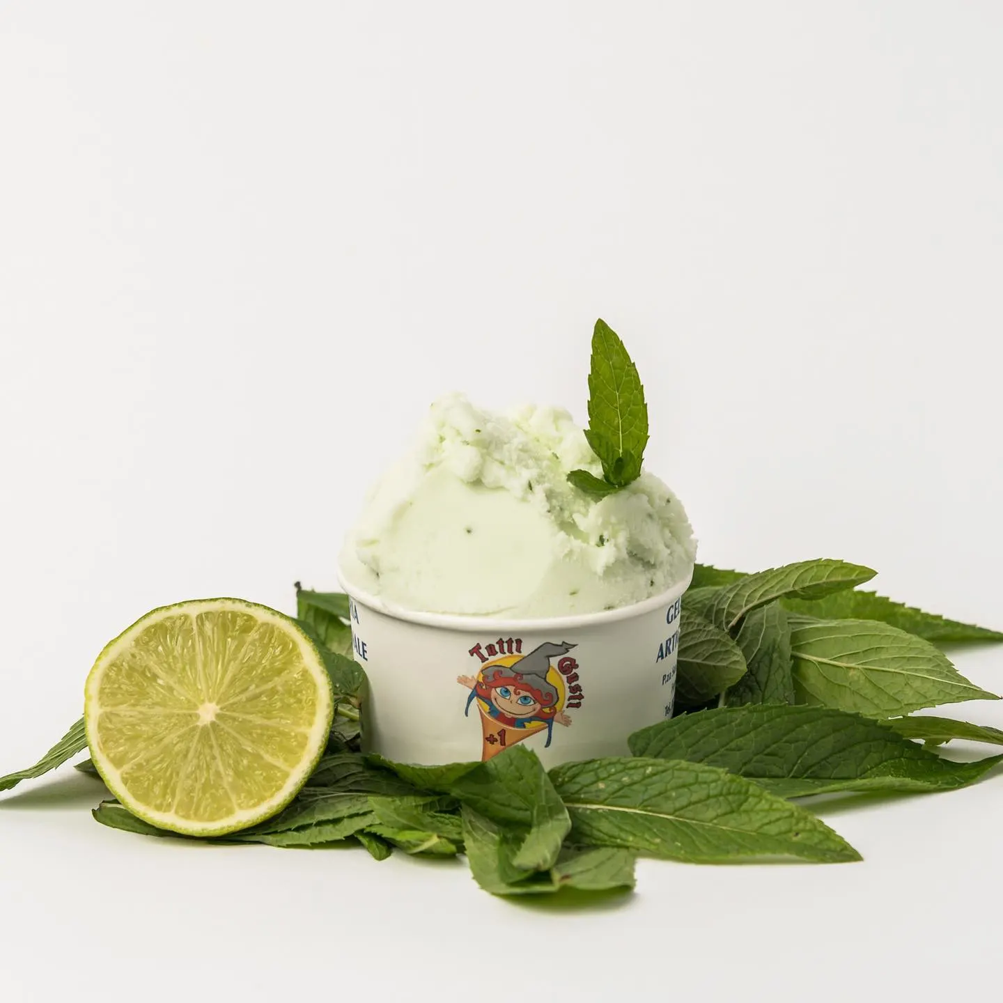 Coppetta di gelato al mojito con mezzo lime e foglie di menta fresca su fondo bianco