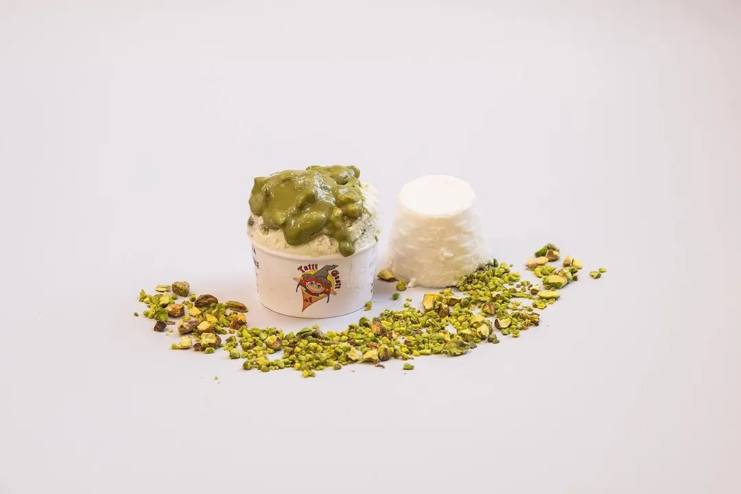 Coppetta di gelato ricotta e pistacchio con crema al pistacchio, una ricotta fresca e granella su fondo chiaro