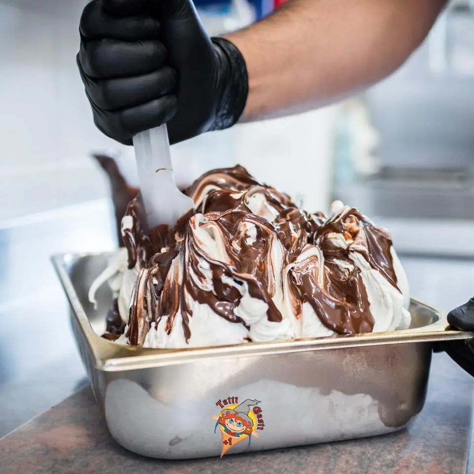 Mano guantata che variega con il cioccolato una vaschetta di gelato Vanitella
